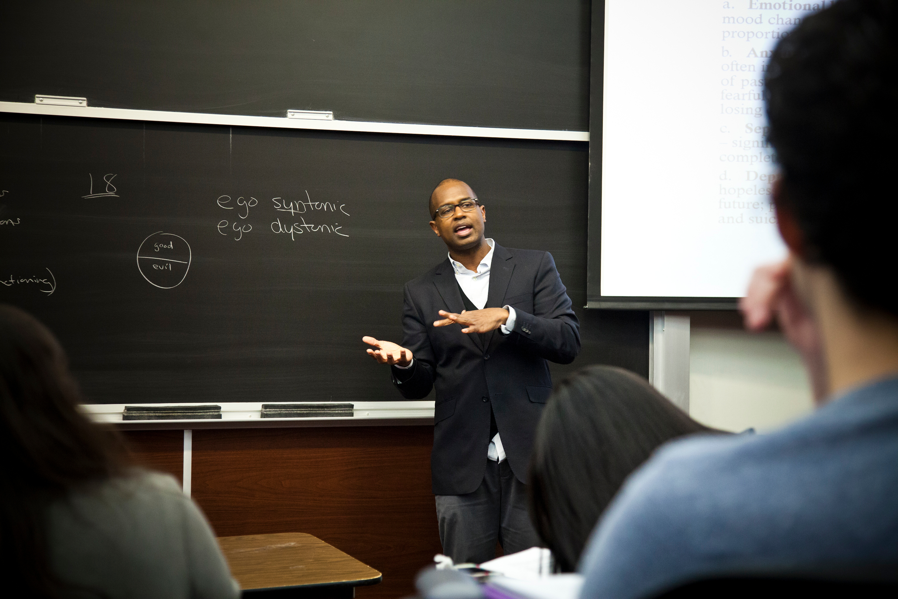 Instructor standing in front of a whiteboard before students in a classroom