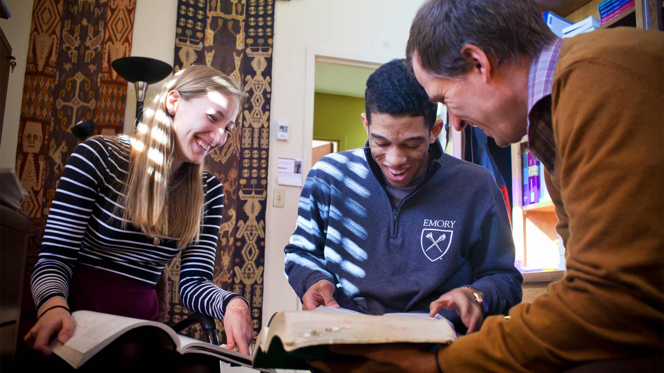 Instructor and two students looking at books in an office