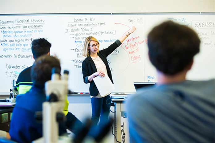 Instructor standing in front of a whiteboard before students in a classroom